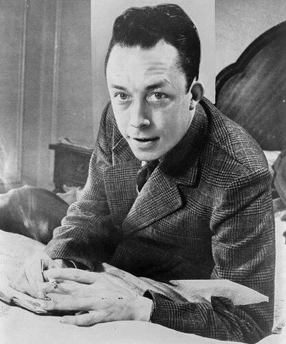 Albert_Camus,_gagnant_de_prix_Nobel,_portrait_en_buste,_posé_au_bureau,_faisant_face_à_gauche,_cigarette_de_tabagisme